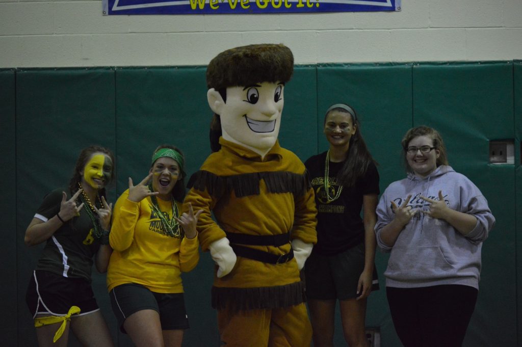 Students dressed in green and yellow stand with the Mountaineer mascot
