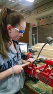 A female student uses a machine to shape a piece of wood